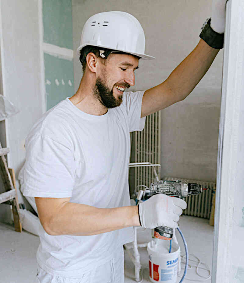 Handwerker mit Helm und Akkuschrauber bei der Arbeit auf einer Baustelle | Symbolbild